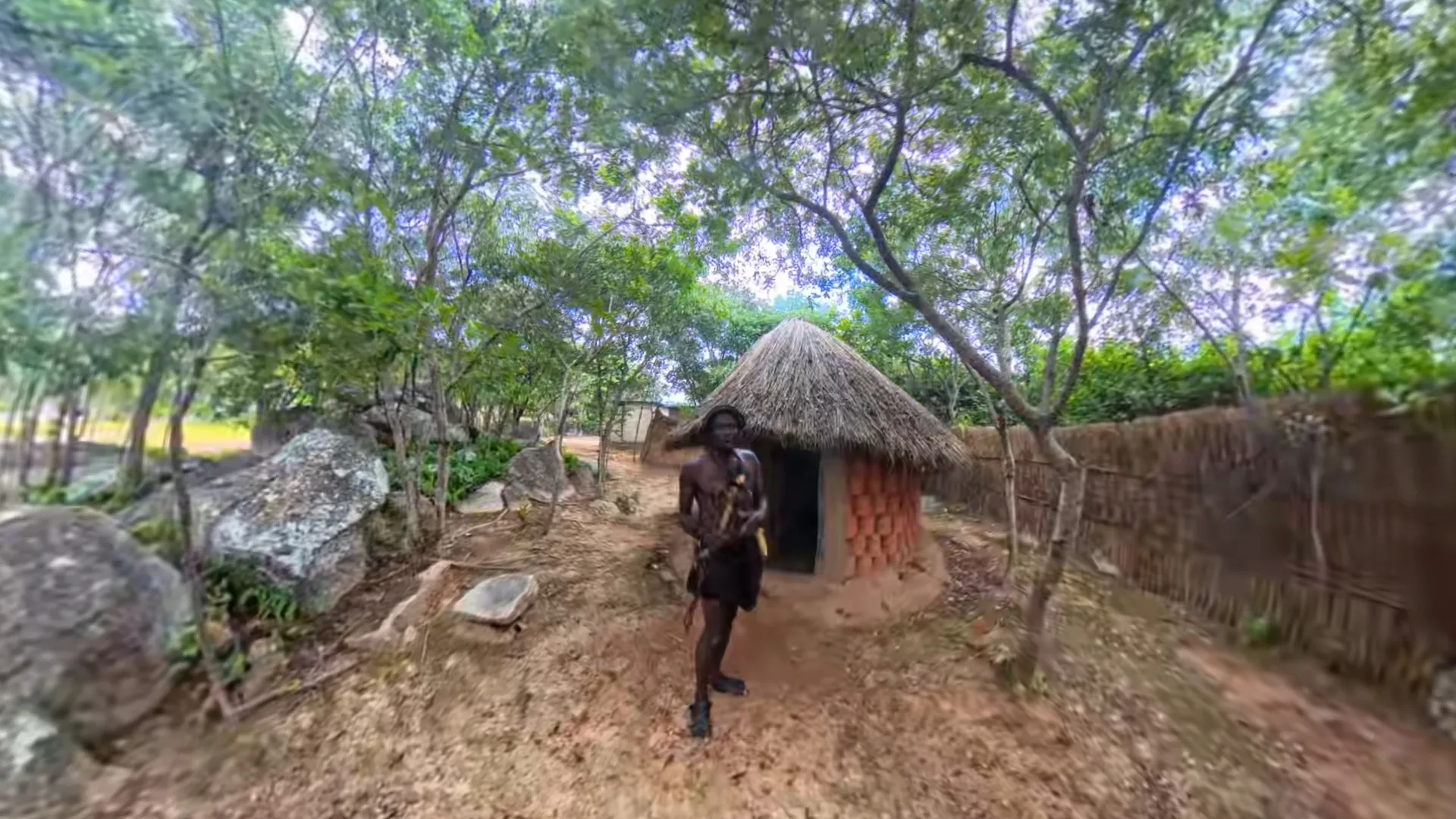 Trymore Ngolanga walking the path beside a thatched hut at paMusha